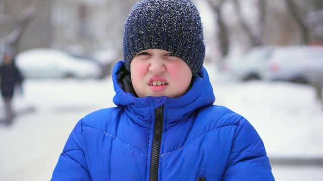 穿着蓝色羽绒服的少年扔雪。冬天，飘落的雪，特写视频素材