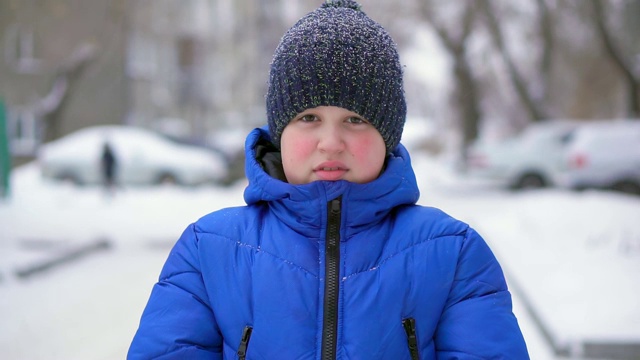 穿着蓝色羽绒服的少年扔雪。冬天，飘落的雪，特写视频素材