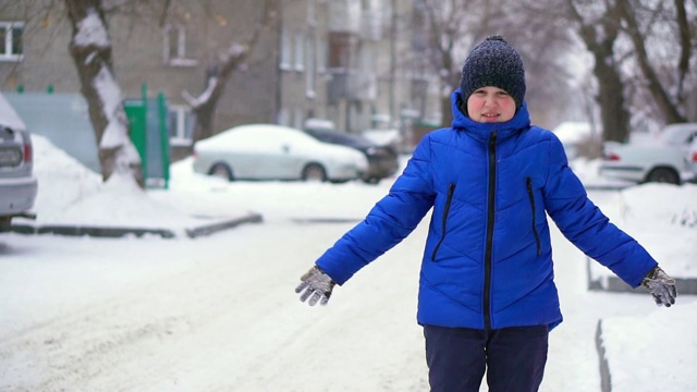 穿着蓝色羽绒服的少年扔雪。冬天,雪花飘落视频素材