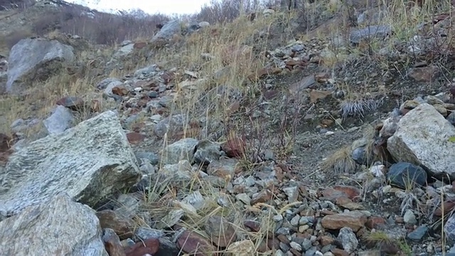 一名男子在山上的岩石上行走，拍摄一段以雪山山峰和冰川为基础的视频视频素材