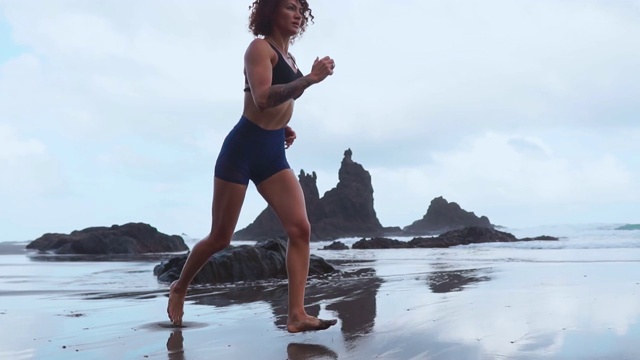 女孩在海洋上的黑色火山沙上奔跑的慢镜头视频素材