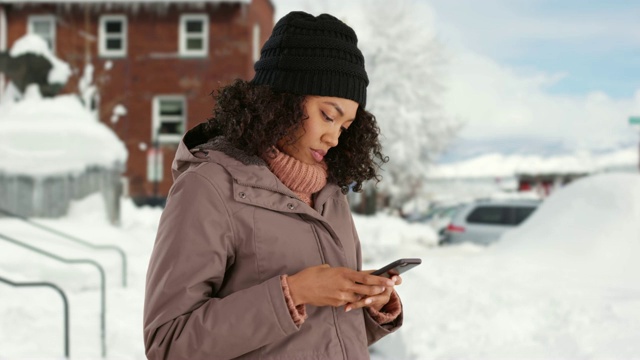 漂亮的黑人女性脱下手套，在外面的雪地里用手机发短信视频素材