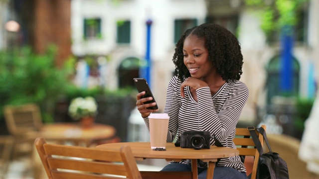 迷人的黑人女人坐在户外cafŽ在威尼斯用智能手机发短信视频素材