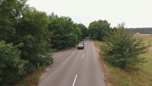 一辆黑色轿车在乡村公路上行驶，人们乘坐的汽车从无人机中射击视频素材