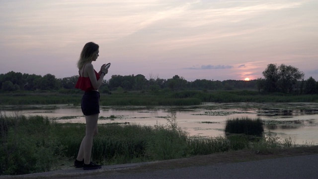 迷人的小女孩在夕阳的背景下拨打电话孤独的女孩走在沼泽附近女人正在用手机打电话视频素材