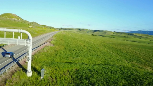 美丽的航拍背景，高速公路通过和平的草原山丘和遥远的山脉与晴朗的天空。视频素材