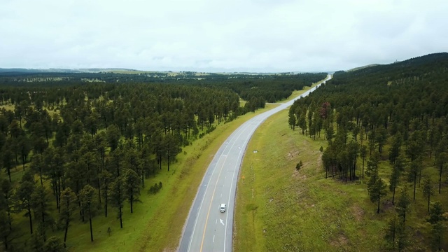 无人机飞过空旷的公路中间美丽的野生绿树林山，白色的汽车行驶着。视频素材