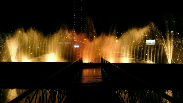 令人惊叹的舞蹈喷泉和喷泉的水在晚上在度假城市-颜色反映在桥和音乐的夜晚表演视频素材