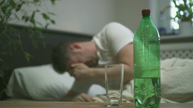 喝着矿泉水，饱受宿醉之苦的男人。视频素材