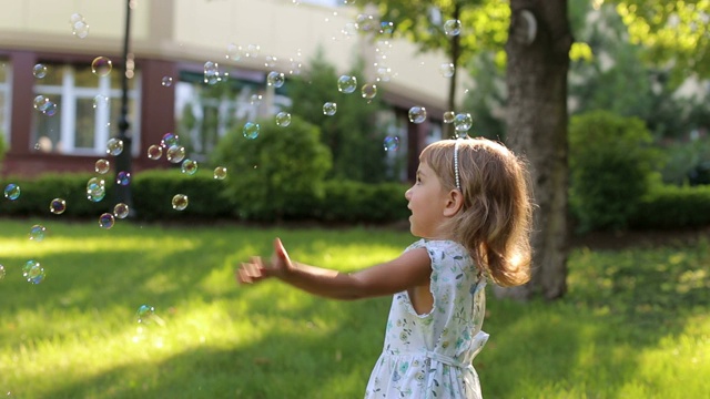 一个可爱的小女孩穿着夏装在公园里玩肥皂泡视频素材