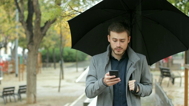 一名沮丧的男子在雨天查看手机上的天气应用视频素材