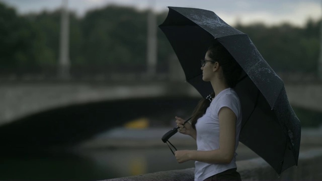 悲伤的女孩撑着伞站在小河旁的小桥后面，想着什么，雨停了，在户外视频素材