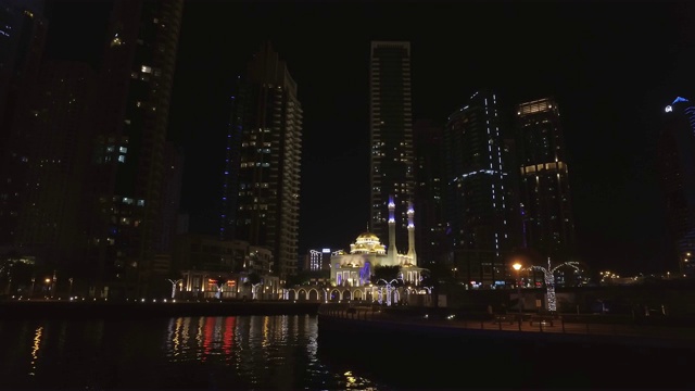 迪拜码头上宏伟的小清真寺的夜景，从漂浮的游船上看视频素材