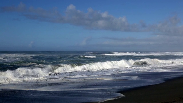 宽阔的镜头，海浪撞击海滩在黎明与海岬的背景和雾上升的沙子。视频素材