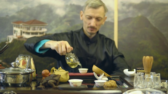 茶道。师傅将绿茶从玻璃茶壶中倒进白杯子里视频素材