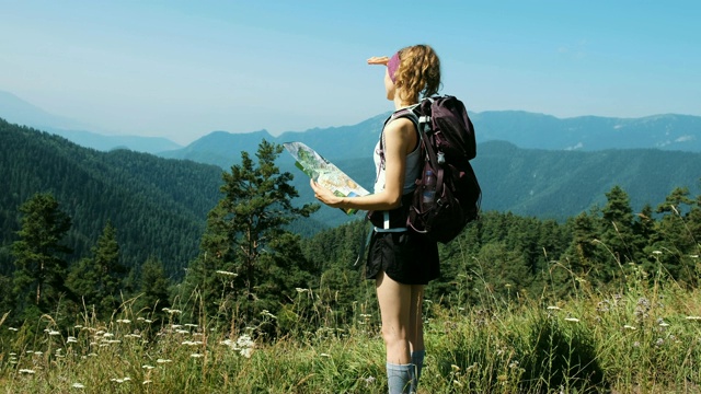 一个背包女游客站在美丽的风景面前，拿着一张纸地图望向远方。女孩在寻找路线视频素材