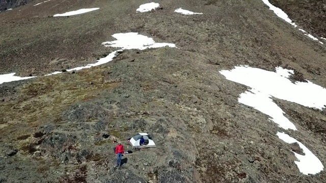 无人机:两个男人和一个帐篷在雪山上，靠近冰冻的湖视频素材