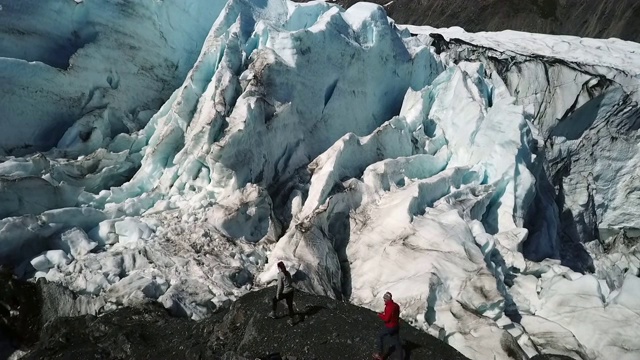 无人机:人们在雪山附近的黑岩石上徒步旅行视频素材