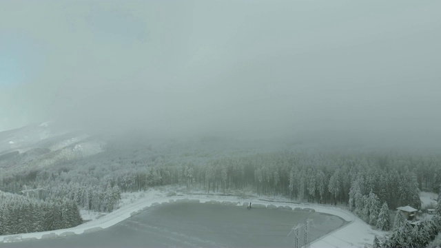 在白雪覆盖的薄雾山林上空飞翔。视频素材