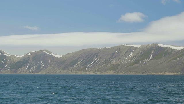 航行游艇漂浮在蓝色的大海上，雪山和明亮的天空景观视频素材