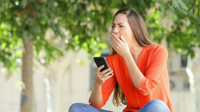 女人用智能手机打哈欠视频素材