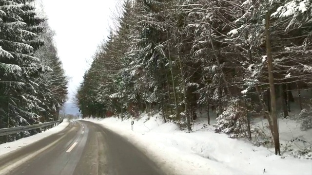 在寒冷的冬天的早晨，在积雪的路上穿过森林视频素材