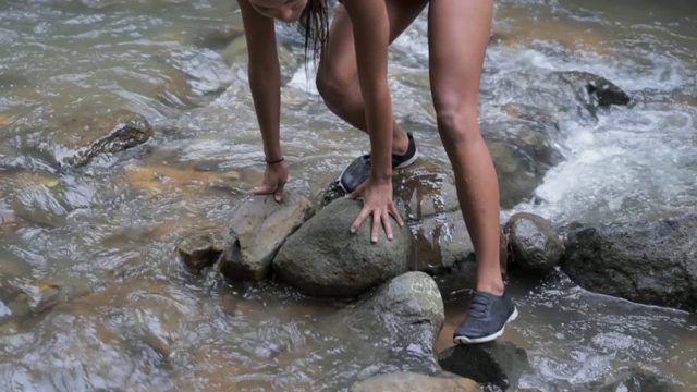 慢镜头:美女爬在溪流中的岩石上的特写视频素材