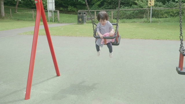 初学走路的女孩在春天的操场上玩秋千视频素材