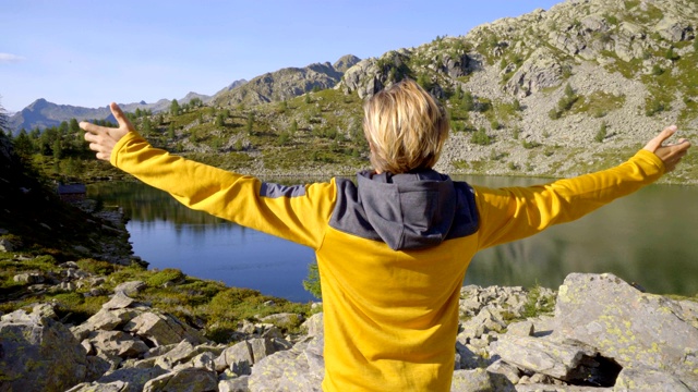 年轻男子徒步旅行在夏天通过惊人的高山湖泊手臂伸出庆祝个人目标。年轻人张开双臂，站在大自然中视频素材