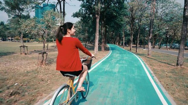 美丽的女孩，她在公园的自行车道上快乐地骑车。视频素材