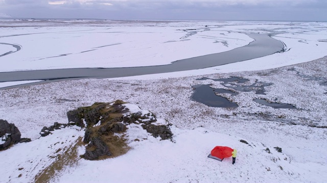 在冰岛偏远地区，一名妇女在白雪覆盖的小山上调整露营帐篷视频素材