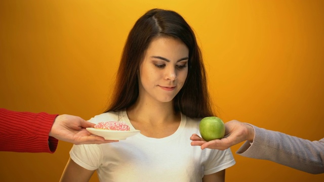 女孩吃苹果而不是甜甜圈，吃健康的零食和维生素而不是含糖食物视频素材