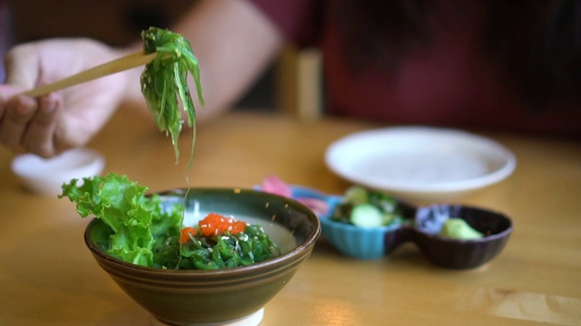 慢镜头年轻女子手拿筷子吃裙带菜沙拉在日本餐馆。视频素材