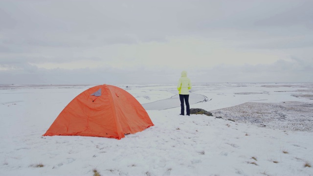 在冰岛，一名妇女站在偏远的、白雪覆盖的风景中的露营帐篷外视频素材