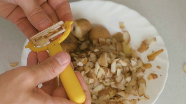 男人的手正在用黄色的削皮器削土豆。视频素材