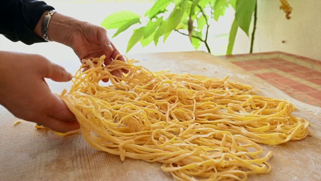 一名妇女正在制作新鲜的意大利面，用新鲜的鸡蛋和硬质小麦面粉制成，被称为“宽面”。宽面是一种在罗马和托斯卡纳美食中很受欢迎的厚而平的意大利面。视频素材