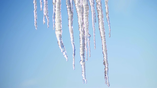 冬天，结霜，多雪，阳光明媚。特写镜头，巨大的透明冰柱悬挂在屋顶上，映衬着天空视频素材