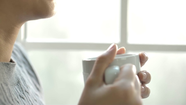 年轻女子享受她的早晨咖啡或茶，看着窗外的阳光视频素材