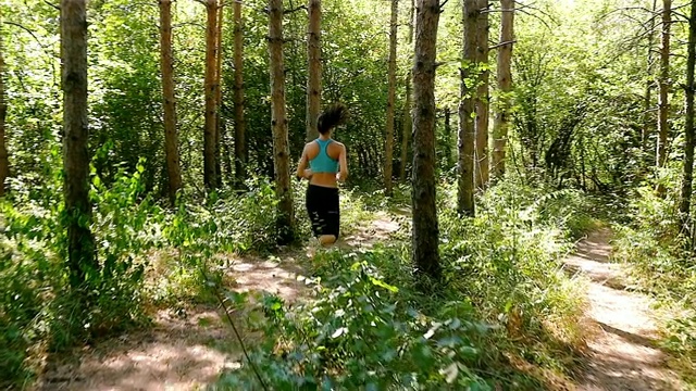 跟踪摄像头拍摄的女子在公园、树林、森林里跑步慢跑的慢镜头视频素材