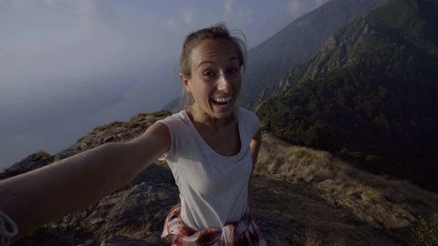 一名兴高采烈的年轻女子一路登山到达山顶后在山顶自拍;人们享受夏日户外活动理念视频素材