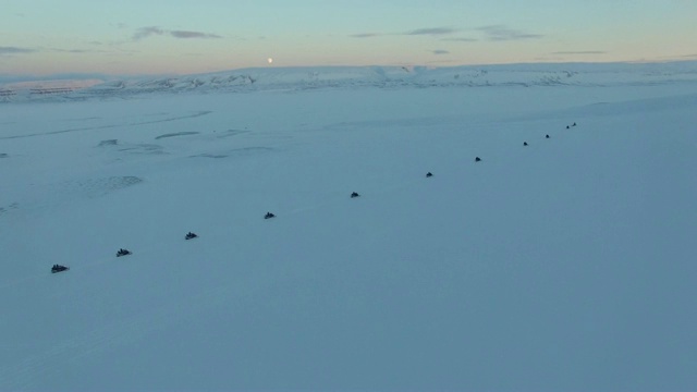 夕阳西下，雪地摩托上的人们排成一行，非常宽的镜头视频素材