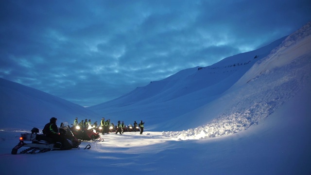 雪地车队在北极山谷的黄昏，车头灯在雪地上视频素材