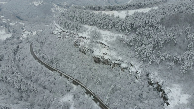 鸟瞰图转向公路在山区冬季积雪覆盖森林视频素材