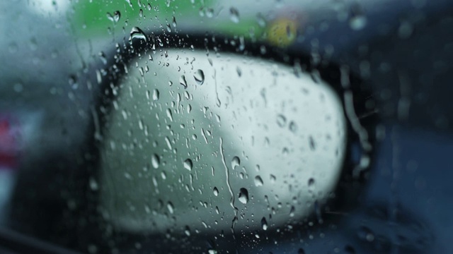 近距离拍摄的镜子上的雨滴。雨中的城市在车镜中暗反射视频素材