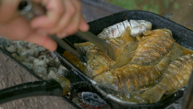 用油煎锅煮鱼，然后烤。在露天炸鱼。专业的餐饮。美味脆的食物。用钳子煮，把盘子翻过来视频素材