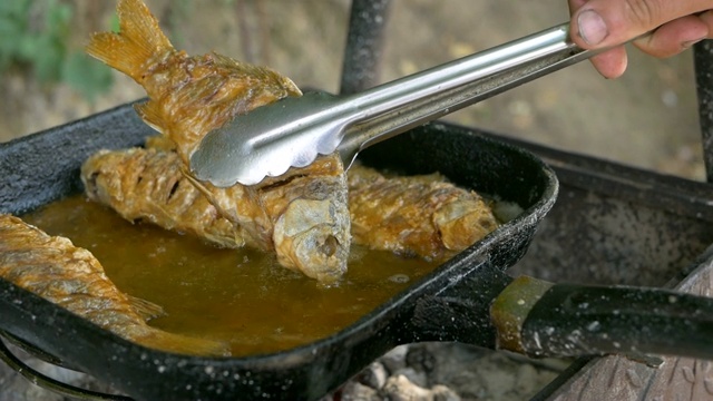 用油煎锅煮鱼，然后烤。在露天炸鱼。专业的餐饮。美味脆的食物。厨师用钳子把做好的盘子放在盘子里视频素材