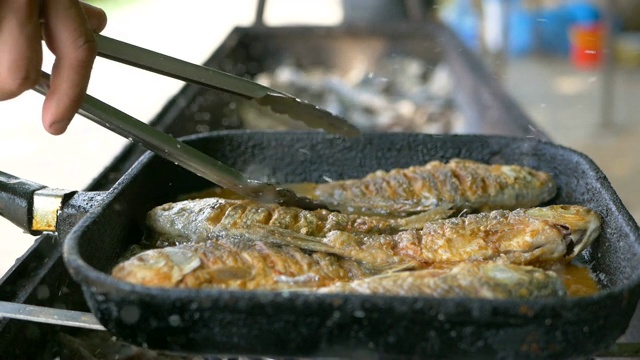 用油煎锅煮鱼，然后烤。在露天炸鱼。专业的餐饮。美味脆的食物。用钳子煮，把盘子翻过来视频素材