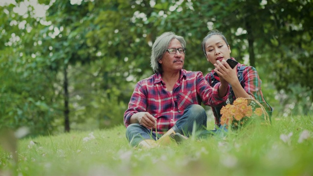 快乐的亚洲成熟夫妇与智能手机自拍，花时间一起在公园户外视频素材