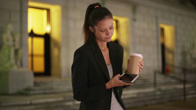 晚上在办公室外面喝咖啡用智能手机的商业女性视频素材