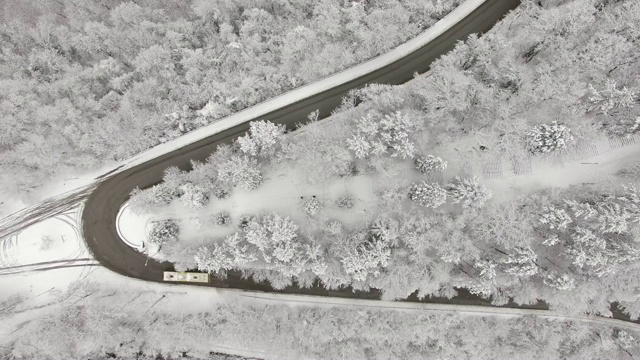 鸟瞰图转向公路在山区冬季积雪覆盖森林视频素材